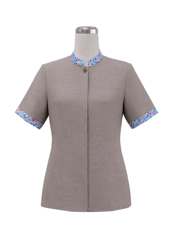 Women's short-sleeve corporate tunic top in taupe grey featuring a standing collar, single accent button, covered placket, and vibrant blue and orange floral trim along the collar and sleeve cuffs, designed by Modoleen Singapore for clinic, spa, and receptionist uniform programs.
