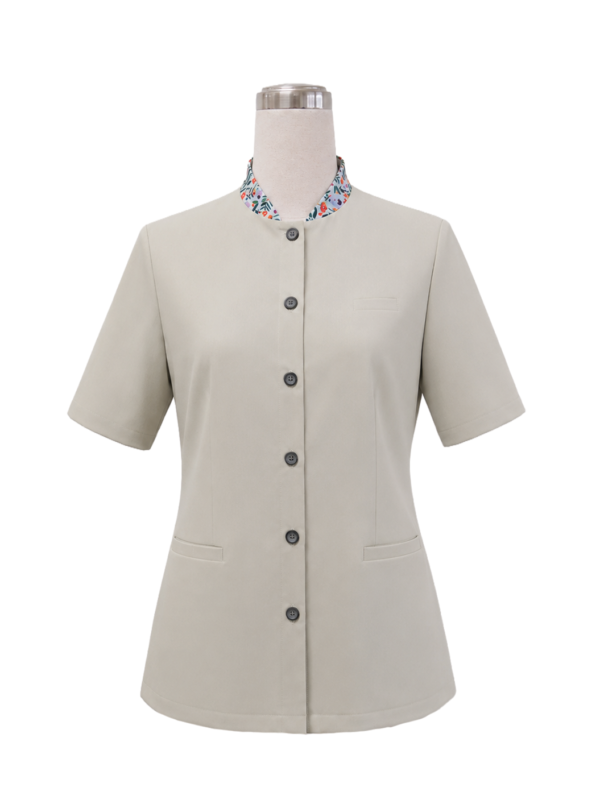 Women's short-sleeve corporate uniform tunic in light cream beige featuring a standing collar with colorful floral inner lining, front button closure, and hip welt pockets, designed by Modoleen Singapore for clinic, spa, and receptionist uniform programs.