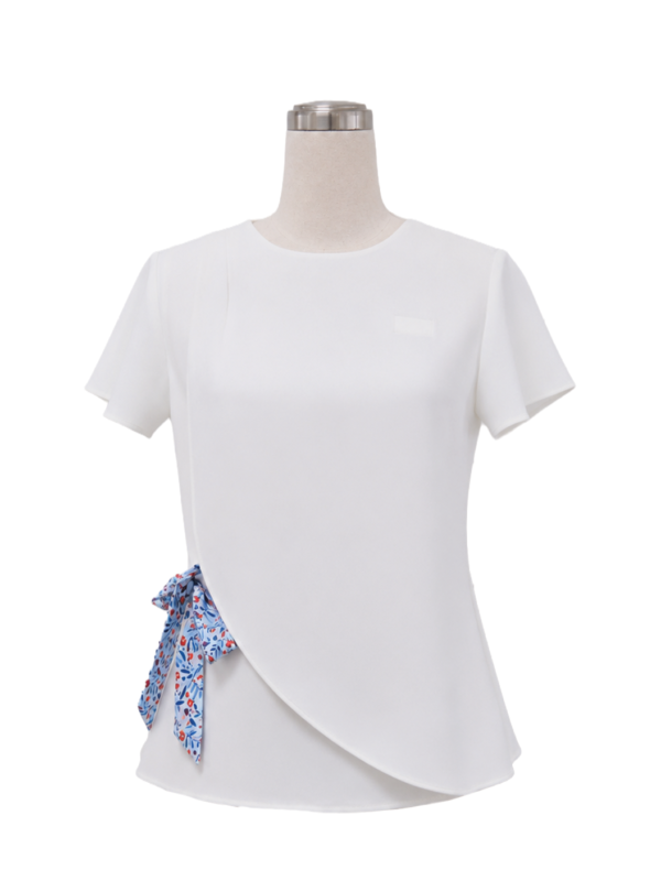 Women's tailored short-sleeve corporate uniform top in solid white featuring an asymmetric curved wrap front hem and a blue and red floral patterned side-waist bow tie sash, designed by Modoleen Singapore for office wear and hospitality uniform programs.